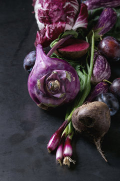 Assortment raw organic of purple vegetables mini eggplants, spring onion, beetroot, radicchio salad, plums, kohlrabi, flower salt over dark metal background. Close up with space