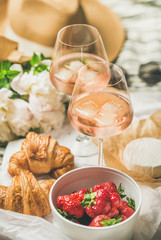French style romantic summer picnic setting. Flat-lay of glasses of rose wine with ice, fresh strawberries, croissants, brie cheese, hat, sunglasses, peony flowers. Outdoor gathering concept