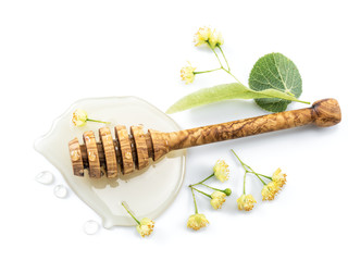 Wooden dipper lays in honey puddle and linden flowers.