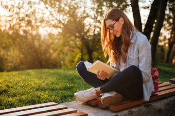 Side view of pleased woman in eyeglasses sitting on bench