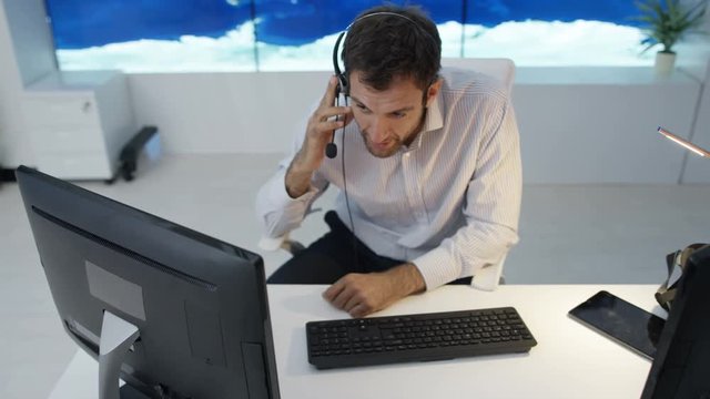  Businessman having conversation via headset with large world map graphic on video wall. Could be global business service agent or airport traffic control room