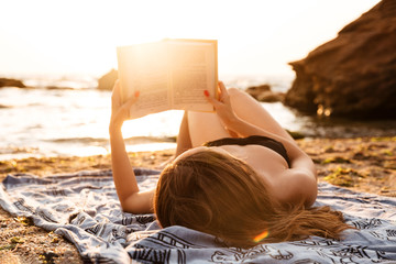 Brunette woman in bikini reading book on beach