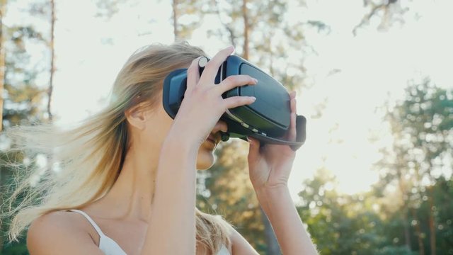 To plunge into virtual reality. A young woman puts on a helmet of a virtual reality in the sun. The wind knocks her hair