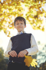 happy schoolboy smiling and holds a leaf in the hand in the autumn on the nature walk outdoors