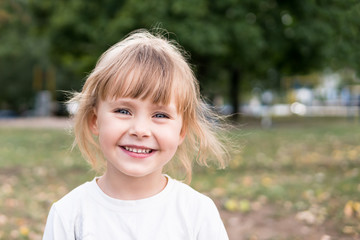 Portrait of a small laughing blond girl in nature with blurred background