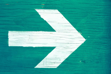 White directional arrow pointing towards right manually painted on a green blueish wooden signboard...