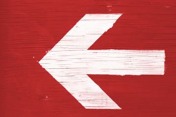 White directional arrow manually painted on a red wooden signboard background. Photo framed...