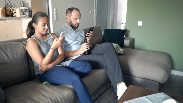 Father and daughter using smartphones sitting on sofa at home
