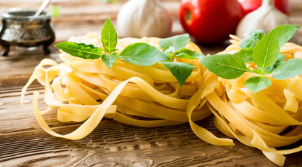 Raw tagliatelle pasta with fresh basil, garlic and tomatos on rustic wooden table