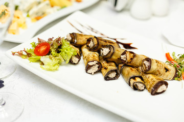 Rustic fried stuffed eggplant with cheese and meat decorated with arugula, tomatoes and sauce on a wooden board