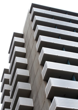 large modern apartment block with external balconies in horizontal pattern with concrete walls and white sky