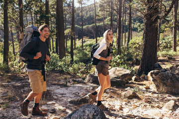 Hiking couple walking in forest wearing backpacks