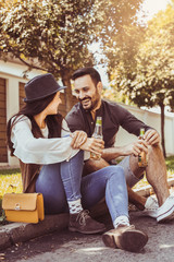 Young couple sitting in park and holding bottle of drink.