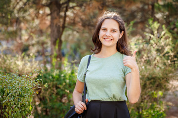 Pretty teenage girl looking at camera, smiling and showing thumbs up outdoors. Portrait of a beautiful girl.