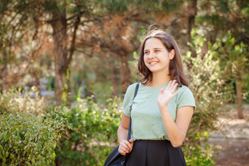 Pretty teen girl smiling and waving her hand outdoors. Portrait of a beautiful girl. Greeting.