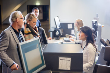Staff Looking At Senior Business Couple At Airport Check-in Desk