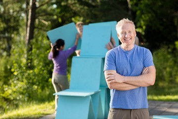 Naklejka premium Mature Man Standing Arms Crossed While Friends Making Planks Pyr