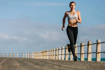 Selbstklebende Fototapeten Sportswoman running on a road by the sea © Jacob Lund
