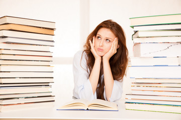 attractive young woman studies wtih hugr book piles on her desk
