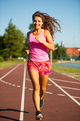 active young woman runs on atheltic track on summer afternoon