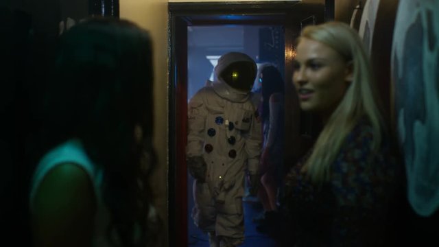  2 girls talking in nightclub, funny astronaut making a move on one of them