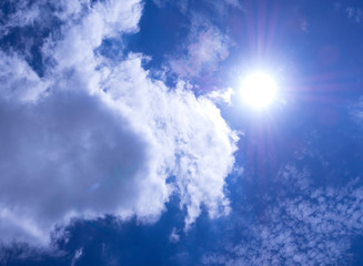 White fluffy clouds in the bright blue sky with light from the Sun