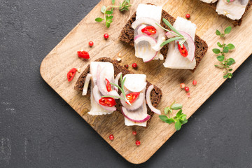 Sandwich with herring, black bread, black background, hot pepper, pickled onion, horizontal, top view