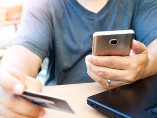 Hands holding credit card and using mobile smart phone for Online payment shopping at on the wood table in the the backyard. online banking concept
