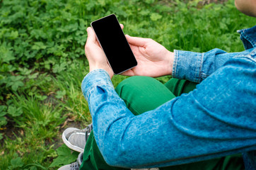  Mobile phone in hands a young hipster business man in denim shirt and green jeans on the background of green grass with paving stone