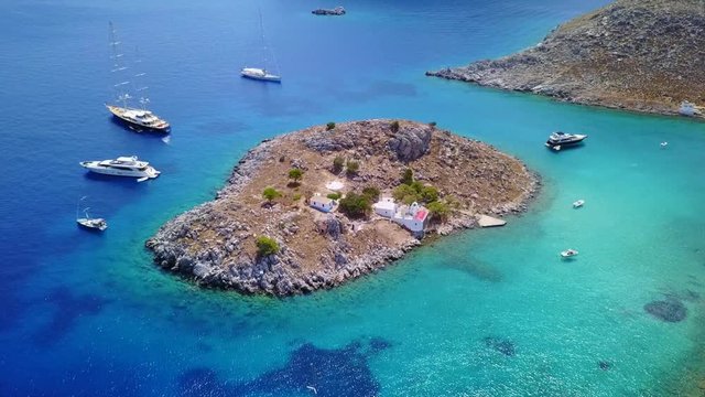 August 2017: Aerial drone video of small heart shaped island with picturesque church of Agia Marina and turquoise clear waters, Symi island, Dodecanese, Aegean, Greece