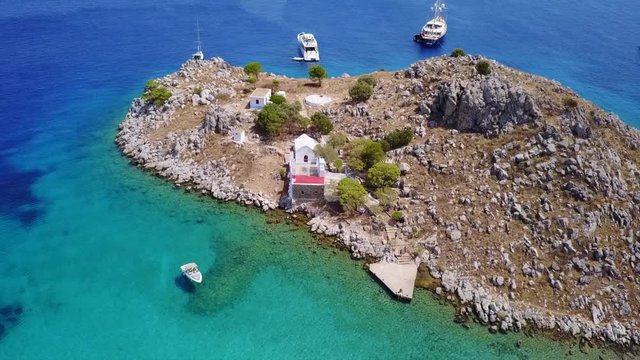 August 2017: Aerial drone video of small heart shaped island with picturesque church of Agia Marina and turquoise clear waters, Symi island, Dodecanese, Aegean, Greece