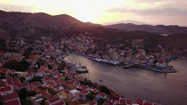 August 2017: Aerial drone video of picturesque island and main port of Symi with traditional architecture and dominant colors at dusk, Dodecanese, Aegean, Greece