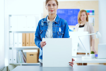 Two young woman standing near desk with instruments, plan and laptop.
