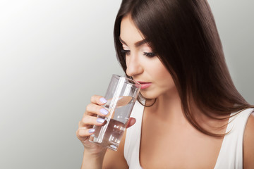 Drink water. Happy young beautiful woman drinking water. A smiling female model holding a transparent glass in his hand. Focus on your hand. On a gray background.