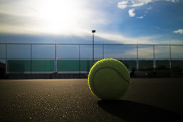 Tennis ball on hard court under sunlight