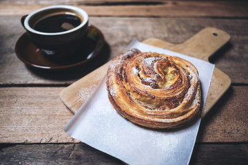 Top view image of a raisin danish and a hot black coffee on vintage wooden table