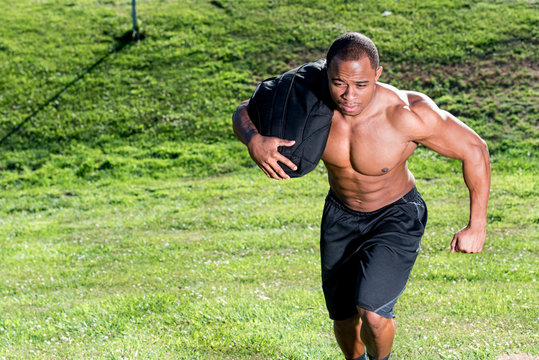 Black sporty young man working out with sandbag while exercises in