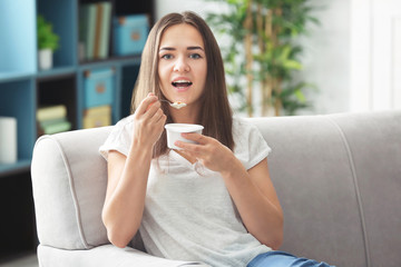 Young woman eating yogurt on sofa at home
