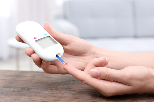 Woman testing glucose level with digital glucometer indoors