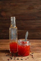 Glass jar and bottle with chili sauce on wooden background