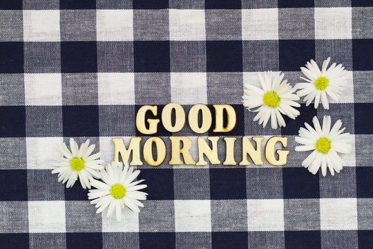 Fototapeta Good morning written with wooden letters on checkered cloth with white daisy flowers  