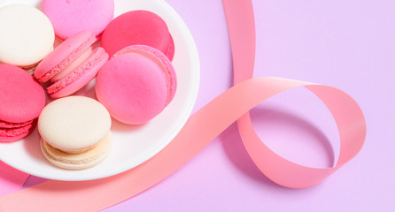 Homemade Colorful macaroons or macaron on White plate with copyspace on pink and purple background