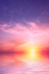 Een paarse zonsondergang met een grote zon met een kleine hoeveelheid wolken boven de zee.