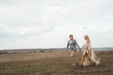 Handsome guy and blonde girl walking on the field, a man leads a woman  holding the hand