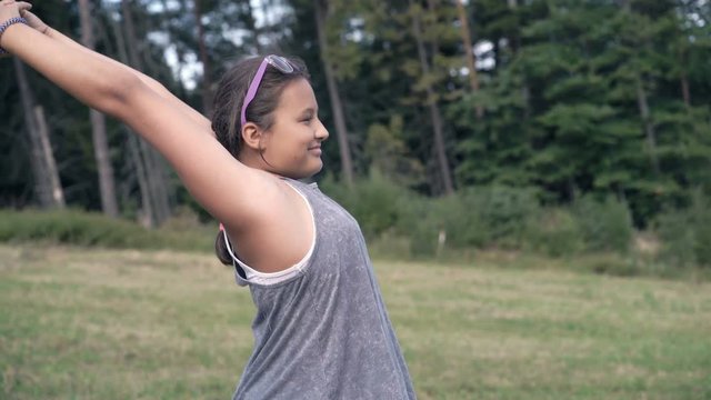 Teenage girl stretching arms standing on field in woods
