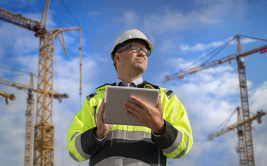 Construction engineer wearing safety vest with yellow crane on the background