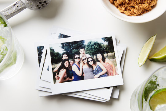 Pile of printed photos with friends in garden posing at camera