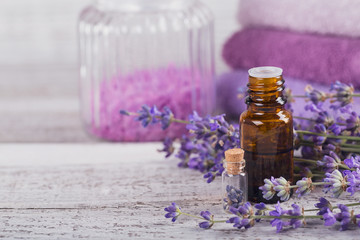 Bottle of essential oil and fresh lavender flowers on a white wooden background. Aromatherapy, spa and wellness concept