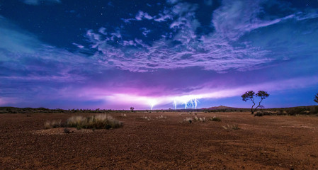 Five lightnings on a cloudy sky full of stars with the red dry soil of the outback desert under it. Thunderstorm lightning.