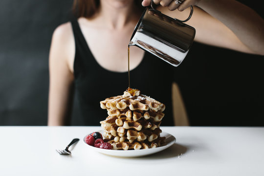 Woman pouring syrup on stack of waffles